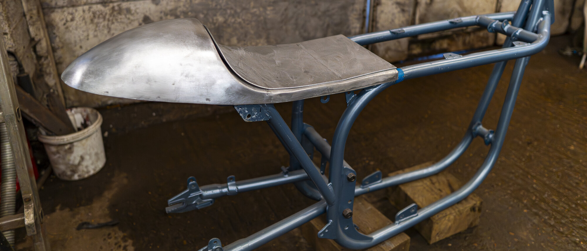 A hand-shaped aluminium tank and seat unit mid-build on a tube frame